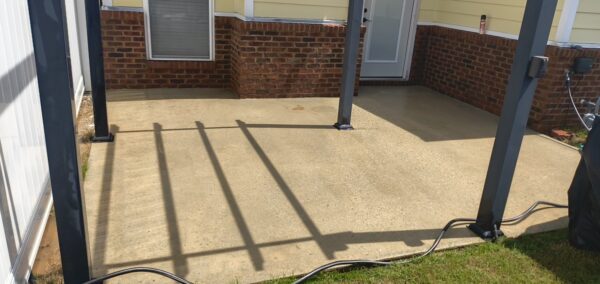 Concrete patio under a covered porch with dark blue metal posts, brick base, and a coiled hose along the edge of the slab.