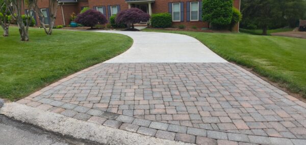 Curved brick-paver driveway leading to a brick house with manicured lawn and shrubs